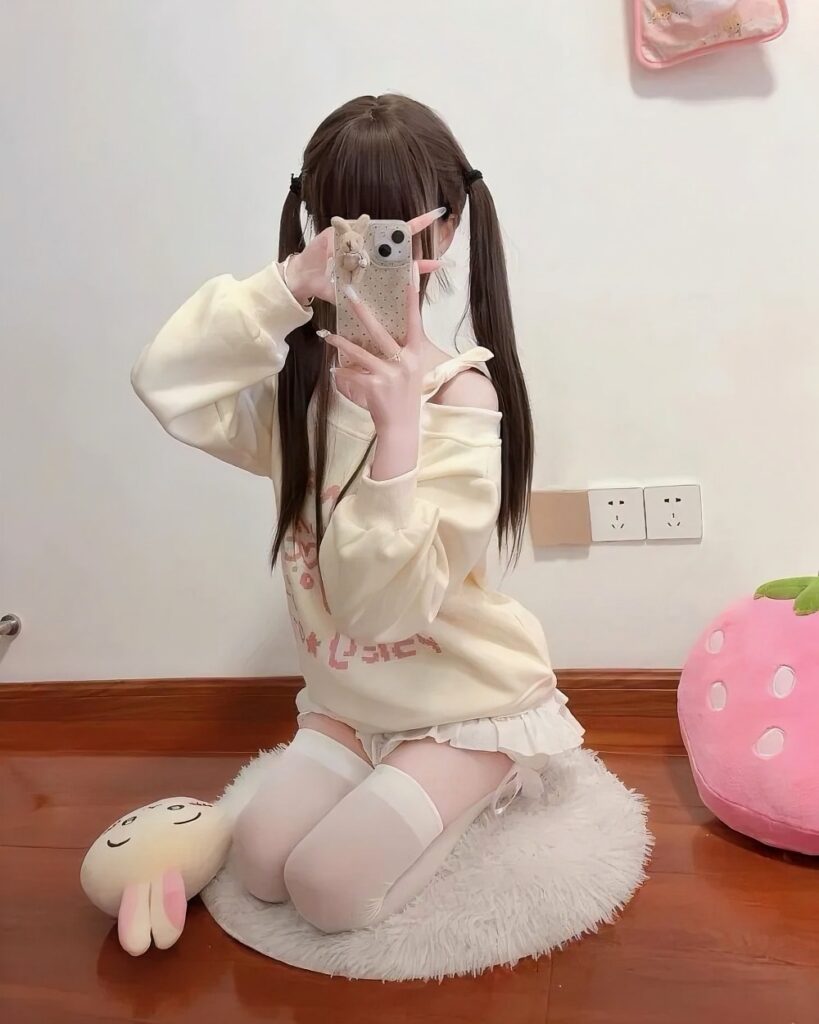 A person wearing a beige nyanko pastel sweatshirt and thigh-high socks, holding a phone.