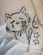 Close-up of a white neko sweater featuring an embroidered cat design with black outlines and a heart.