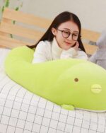 Kawaii animal mochi plushie, light green, resting on a bed with a woman.
