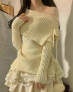 Cream colored one-shoulder knitwear sweater with a ruffled skirt and bow detail.