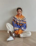 Woman wearing a colorful kawaii winter sweater with tassels and earmuffs, paired with loose-fitting pants and socks.