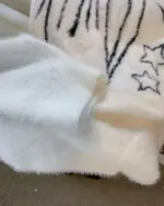 Close-up of a white neko sweater featuring star and paw print designs.