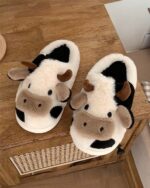 Pair of The Cow Slippers, plush cow-shaped house slippers with ears and spots.