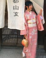 A woman wearing a pink traditional japanese kimono with floral patterns, holding a handbag.