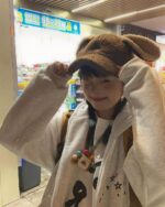 Person wearing a y2k kaomoji hoodie and brown hat in a shopping mall.