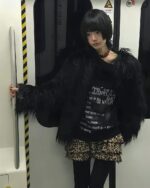 Person wearing a grunge aesthetic sweater, dark pullover with fur trim.