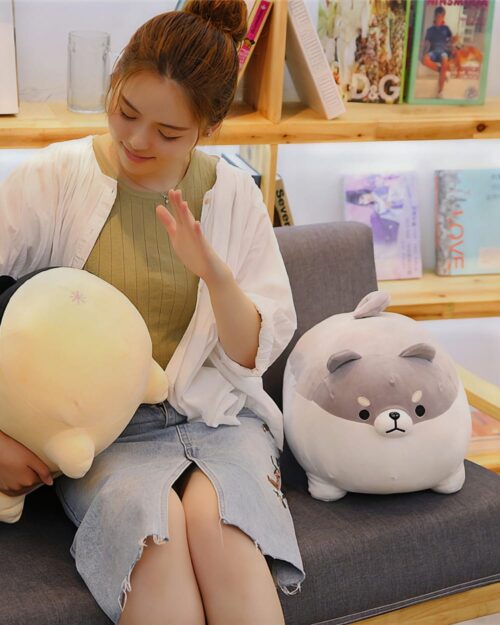 A gray super fat shiba plushie, a chonky dog stuffed animal, sits on a couch.