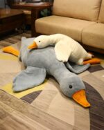 A large, grey big goose plush toy resting on a rug, with a smaller white goose on top.