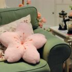 Pink sakura flower pillow resting on a green sofa in a room setting.