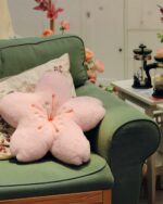 Pink sakura flower pillow resting on a green sofa in a room setting.