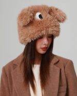 A fluffy eyed hat worn by a woman, featuring plush ears and a large eye.