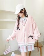 Pink kawaii bow sweater with cable knit details, featuring a black bow accent and layered outfit.