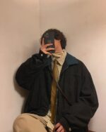 Person holding a phone wearing a korean college jacket, corduroy style.