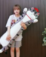 Long cat plushie, Whiskers the Stripped Emperor Cat, held by a person.