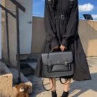 Black gothic lolita dress with straps and layered skirt, carried with a black bag.