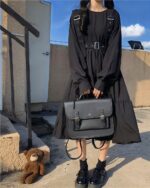 Black gothic lolita dress with straps and layered skirt, carried with a black bag.