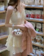 Woman wearing a pale pink lolita french dress with frills, holding a plush teddy bear.