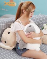 Two big bunny plushies displayed on a couch. One is grey and white, the other is beige.