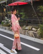 Woman wearing a traditional japanese kimono strolling on a street in Japan, with an umbrella and flowers.