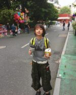 Woman wearing a retro grunge t-shirt stands on a city street with a backpack and drinks.