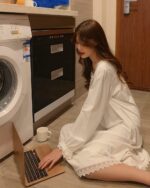 Woman wearing a soft girl aesthetic nightdress, working on a laptop in a home setting.