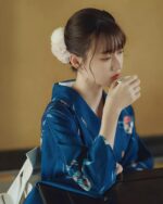 Woman wearing a deep blue yukata with floral pattern, enjoying tea.