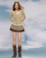 Model wearing a beige vintage aesthetic cardigan over a plaid skirt and boots.