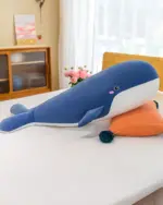 Blue kawaii whale plushie lying on a white surface, with a pink nose and embroidered details.