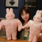 Two pink buff bunny plushies sit on a table with a woman. These soft plushies are a unique buff bunny plushie design.
