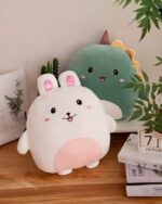Two squishy animal plushies: a white bunny and a green dinosaur, displayed on a wooden table.