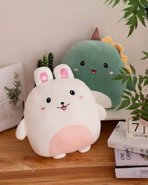 Two squishy animal plushies: a white bunny and a green dinosaur, displayed on a wooden table.