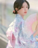 A woman wearing a pastel japanese yukata with floral print, holding a fan.