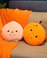 Two kawaii fruit plushie cushions – a peach and an orange – displayed on a couch.