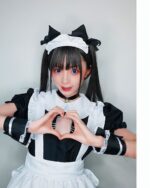 A person wearing a cat maid cosplay outfit, featuring a white and black dress, headband, and heart shape.