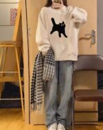 Oversize round neck cat graphic sweater in a casual outfit with plaid scarf and jeans.