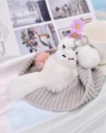 Close-up of a white fox plush keychain, soft and fluffy, with a grey cushion.