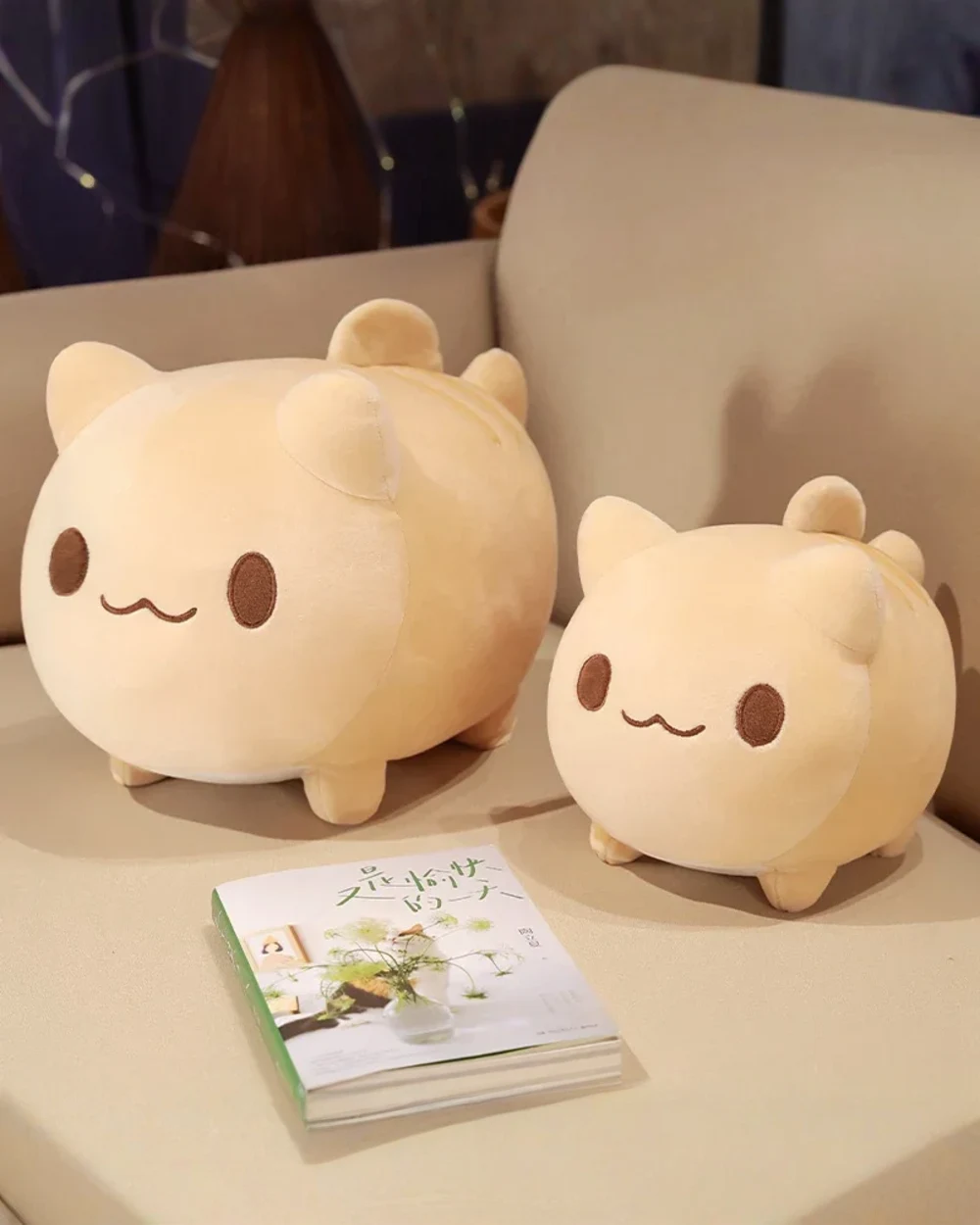 Two soft, light-tan round neko plushies displayed on a table.