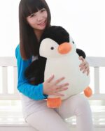 A large, soft, black and white chonky penguin plushie held by a young woman.