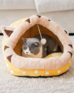A yellow and white kawaii cat bed with brown ears, occupied by a gray cat.