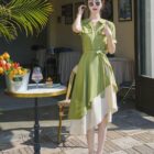 French vintage dress in a light green hue, featuring a belted waist and asymmetrical hemline, worn by a woman.