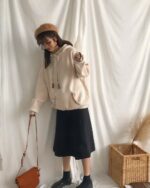 Cream colored ethno-chic hoodie features embroidered details and a drawstring hood, styled with a skirt and bag.