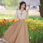 Woman wearing a cottagecore aesthetic dress in a flower field, holding an umbrella.