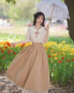 Woman wearing a cottagecore aesthetic dress in a flower field, holding an umbrella.