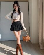 Woman wearing a black pleated corduroy skirt and a cream cardigan. Preppy corduroy skirt style.