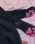 Black cat paw socks on a pink sheet, showcasing the paw print design.