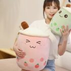 Two bubble tea plushies – pink and green – are held by a woman. Product: bubble tea plushies.