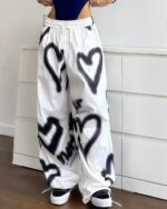 White y2k aesthetic pants with black heart graffiti print. High-waisted loose fit style.