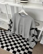 Gray bowed pullover sweater displayed on a hanger with black bow accents.