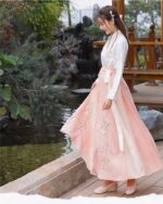 Woman wearing a pink hanfu summer dress with floral embroidery outdoors.