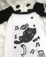 White tee with a black neko cat illustration, featuring musical notes and kawaii details. A playful neko cat t-shirt.